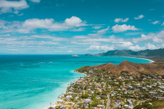 Photo by Jess Loiterton A scenic aerial shot of a tropical town by the ocean with turquoise waters and mountain ranges.