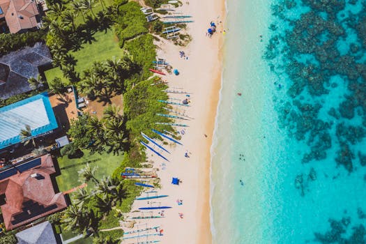 Photo by Jess Loiterton Stunning aerial view of a tropical beach, vibrant blue waters, and lush greenery.