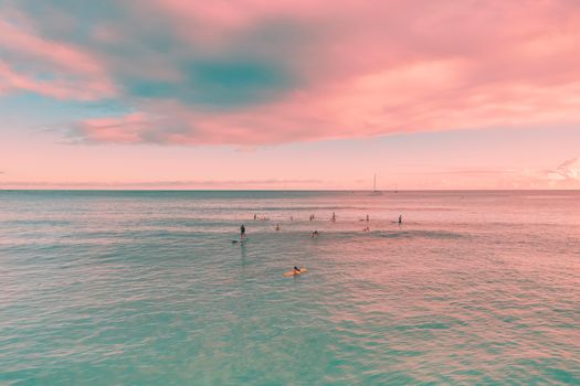 A group of people paddle boarding on a calm ocean under a vibrant pink sunset sky, ideal for relaxation and adventure enthusiasts.
