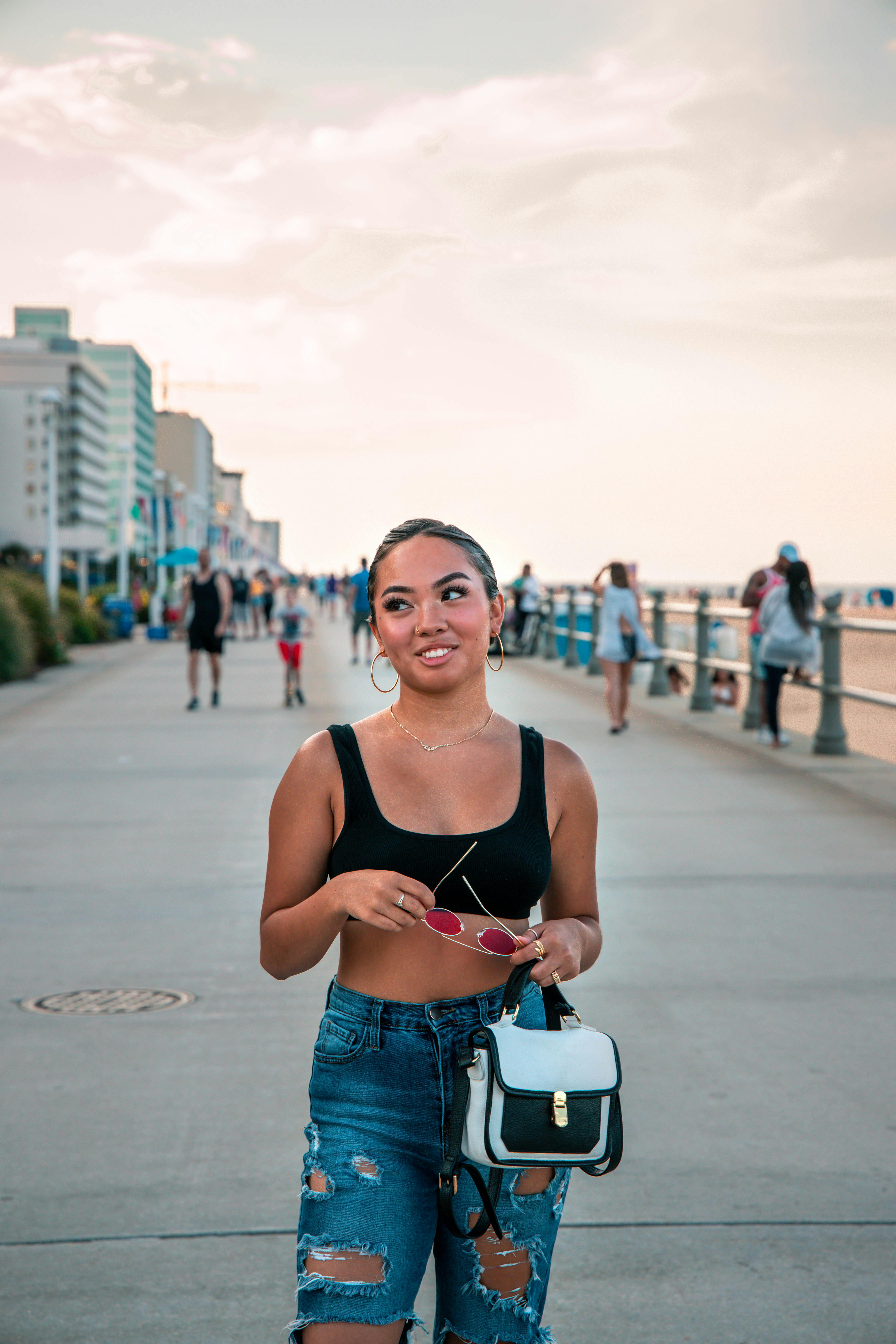 A fashionable young woman walks along a bustling beachfront promenade during sunset.