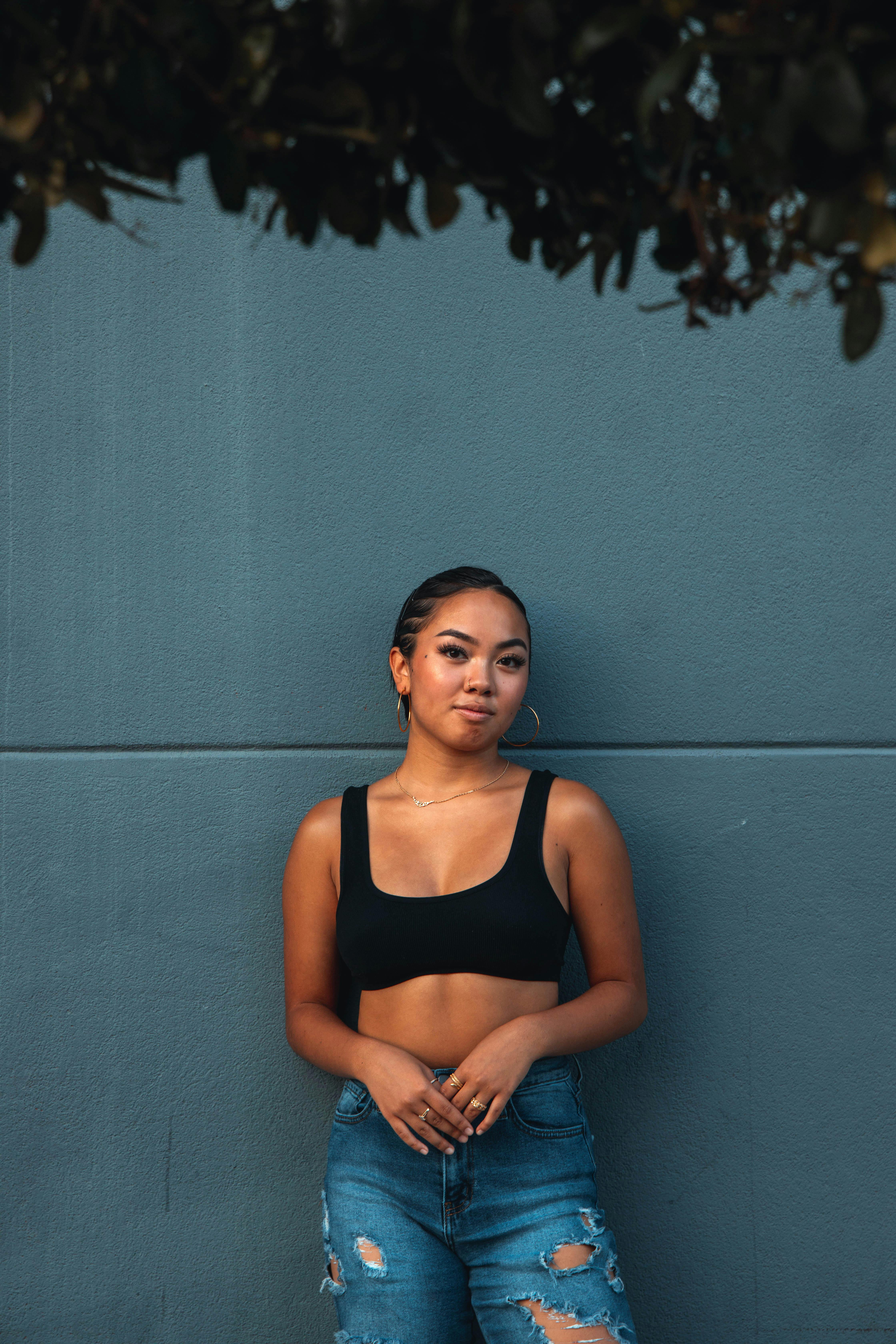 woman in black sports bra leaning on a gray wall while seriously looking at the camera