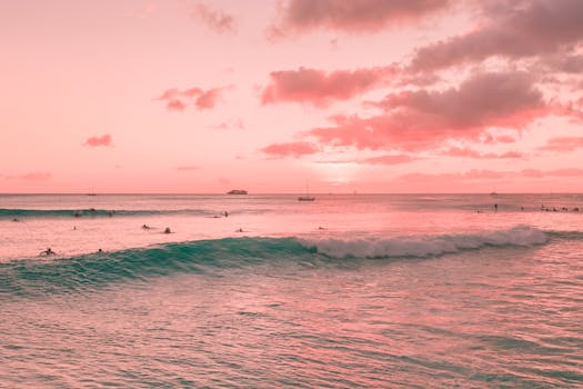 在迷人的粉红色日落天空下，冲浪者骑着柔和的海浪，周围环绕着宁静的海景