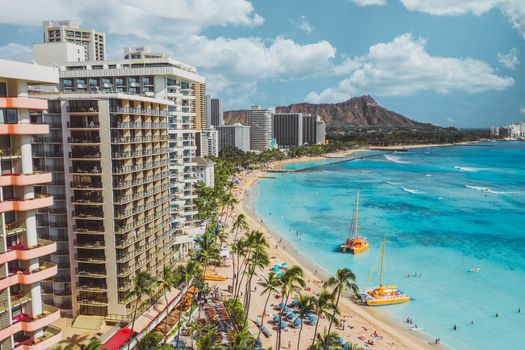 Photo by Jess Loiterton A vibrant aerial view of Waikiki Beach with Diamond Head in the background, showcasing luxury hotels and clear blue waters.