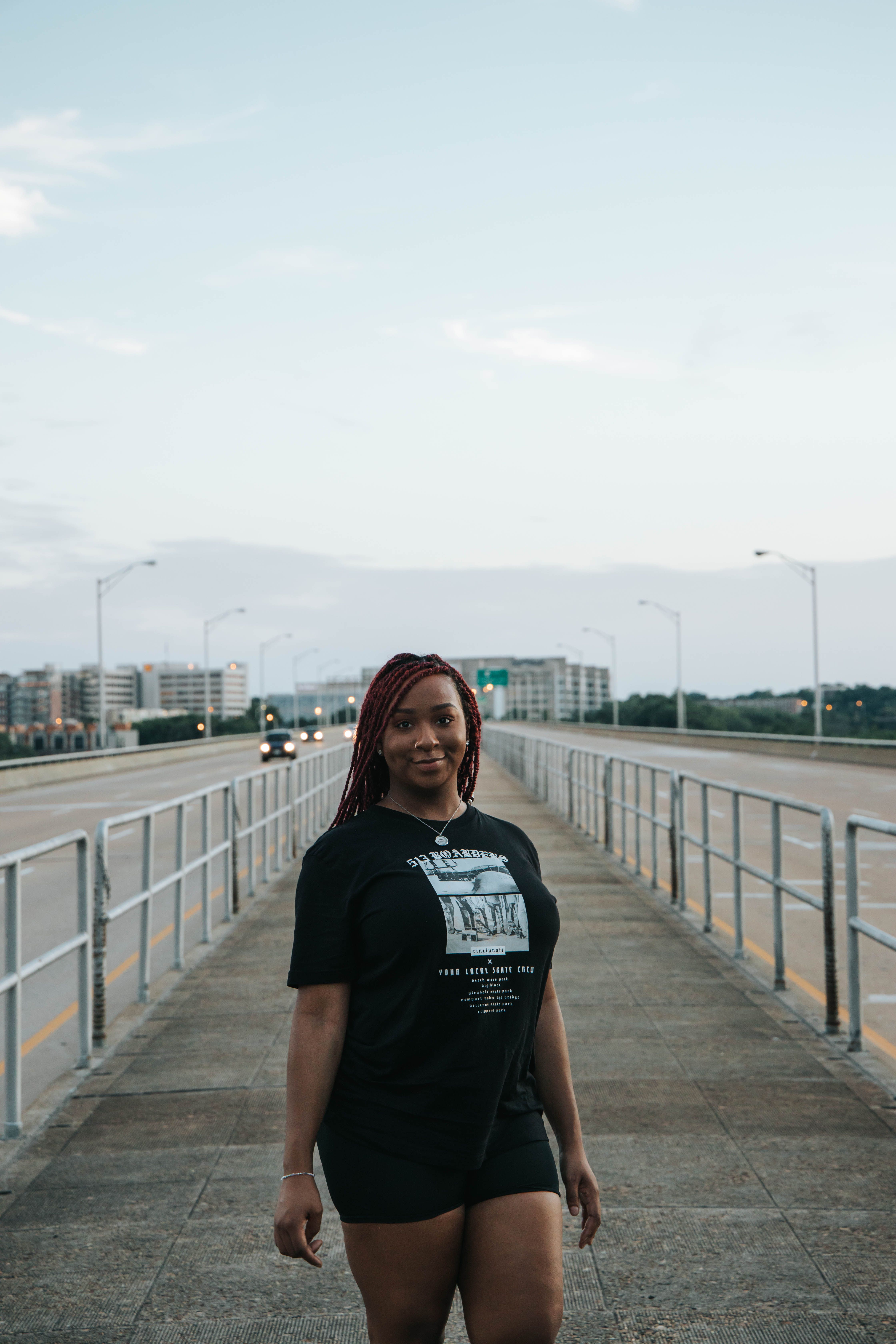 A woman with braided hair walks confidently on a bridge in an urban setting at daytime.