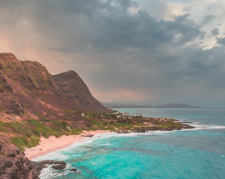 A breathtaking view of a coastal landscape featuring rugged cliffs, turquoise sea, and a cloudy sky.