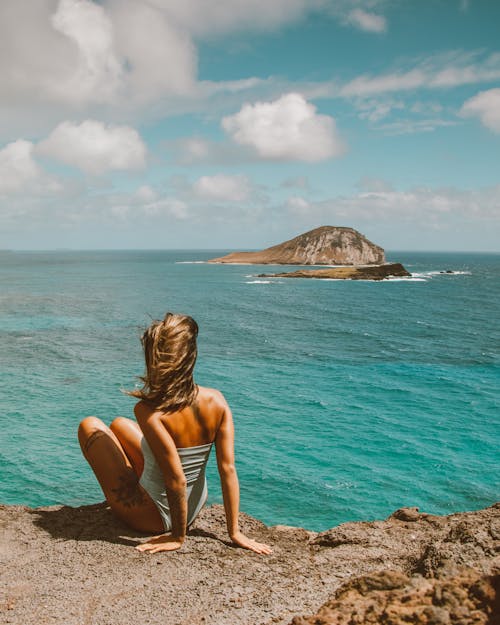 Back View Shot of a Woman Sitting on the Rocky Ground while Looking at the Scenery