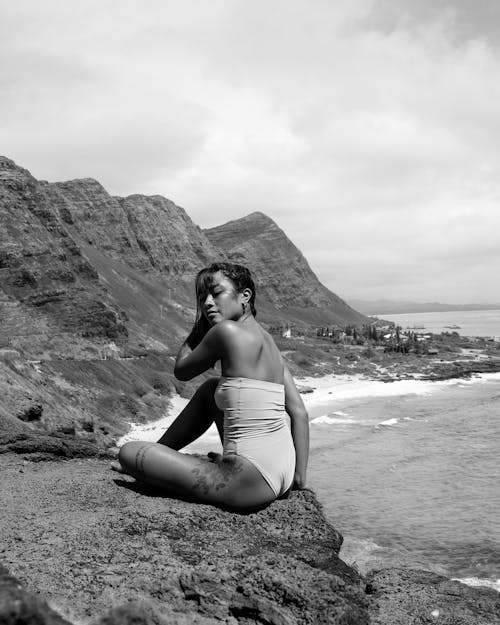 Grayscale Photography of a Woman in Bikini Sitting on the Rocky Ground