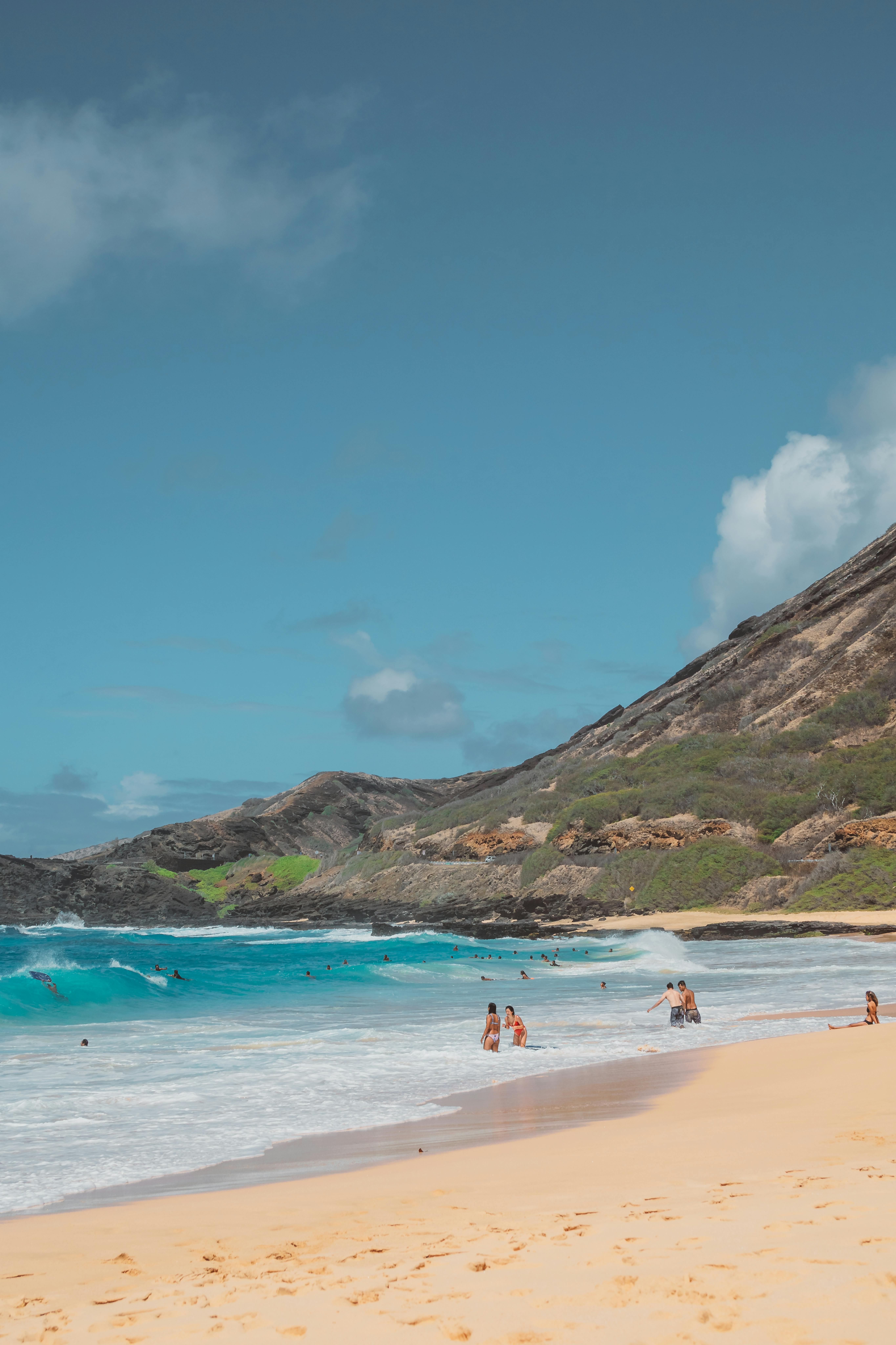 在晴朗的蓝天下，游客们正在风景如画的海滩上享受海浪