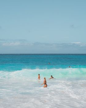 Women enjoying a swim in vibrant ocean waves at a sunlit beach, perfect summer vibe.
