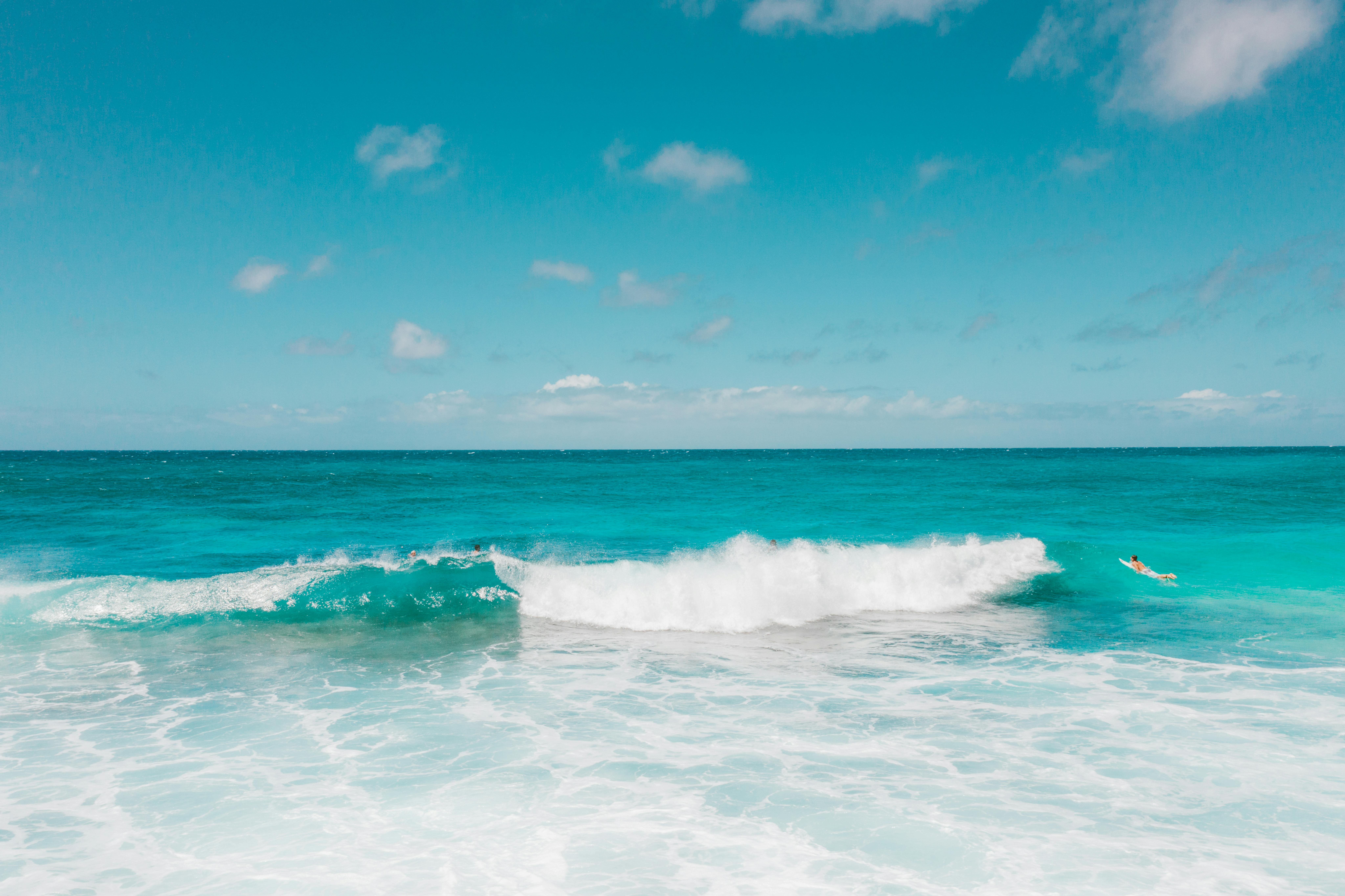 在湛蓝的天空下，冲浪者骑着碧绿的海浪，捕捉着夏季冒险的精髓