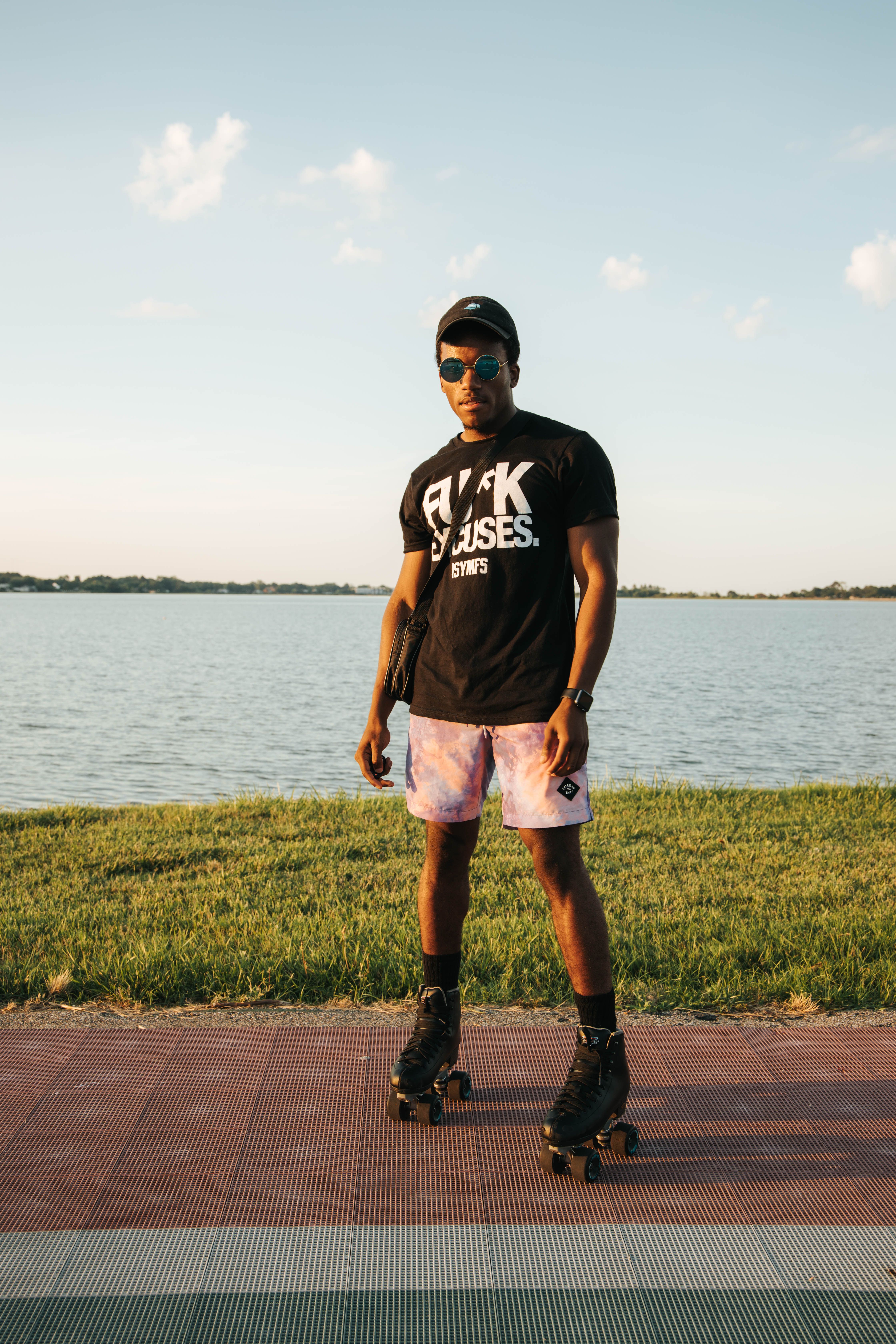 Person roller skating by a lakeside during a summer day, wearing casual attire and sunglasses.