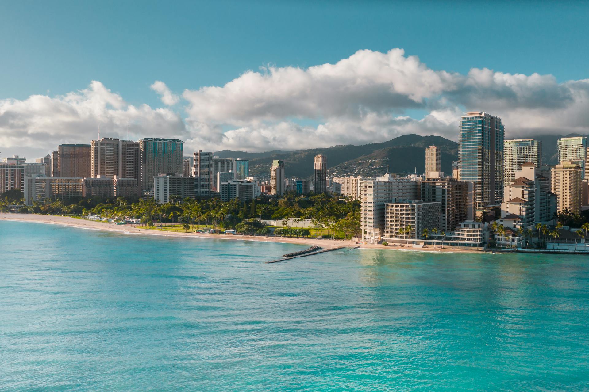 Aerial view of Waikiki Beach with vibrant city skyline, turquoise water, and lush greenery.