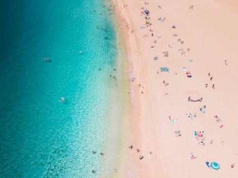 Stunning drone shot capturing a lively beach with people and clear turquoise water.