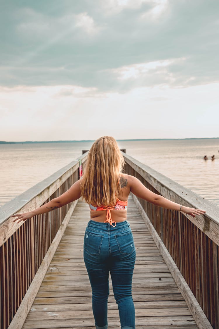 Woman In Blue Denim Jeans Walking On Wooden Boardwalk