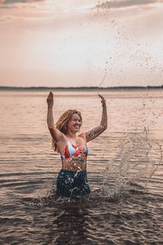 A happy woman joyfully splashing in the ocean during sunset, capturing a moment of pure enjoyment.