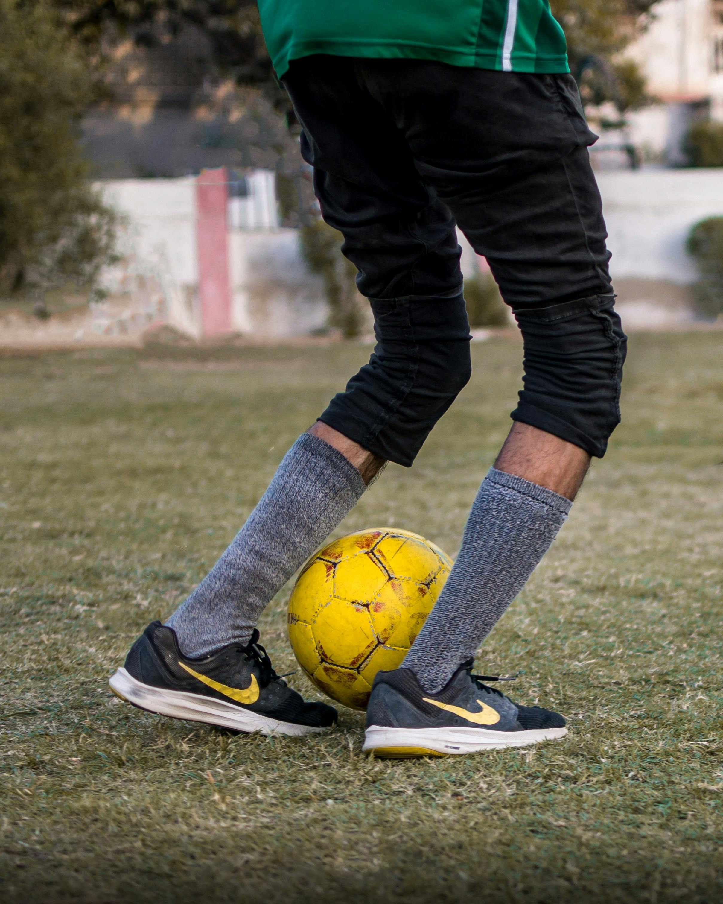 crop male player in sportive cloth kicking soccer ball on grass