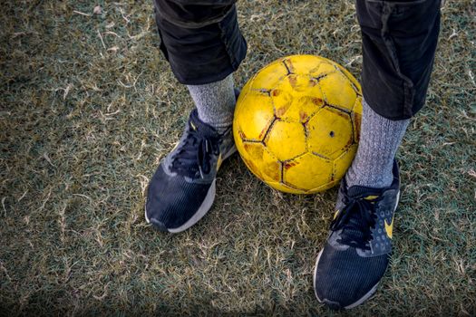 From above of crop faceless person wearing sneakers with socks standing with soccer ball between legs on grass