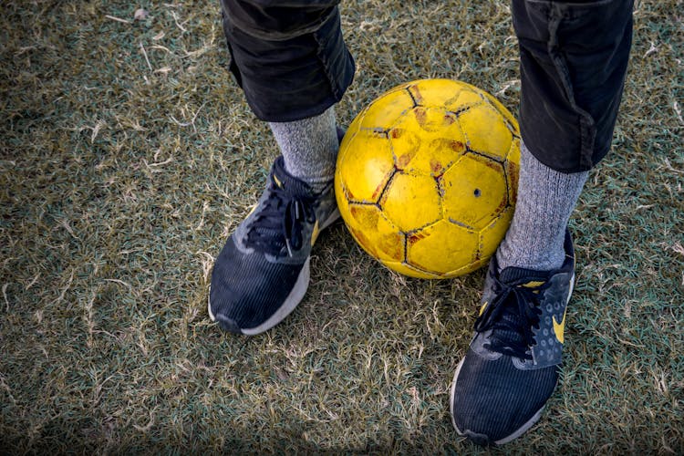 Faceless Person Standing With Soccer Ball Between Legs On Grass