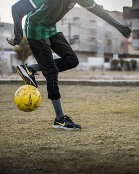 Teen kicking a soccer ball in an urban field, showcasing active lifestyle and sportswear.