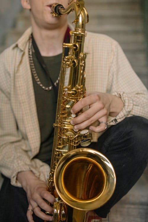 Person in White and Gray Plaid Dress Shirt Holding Saxophone