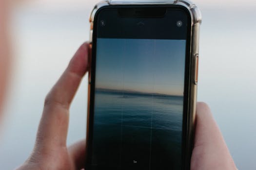 Close-up of a smartphone capturing a serene lakeside view at sunset.