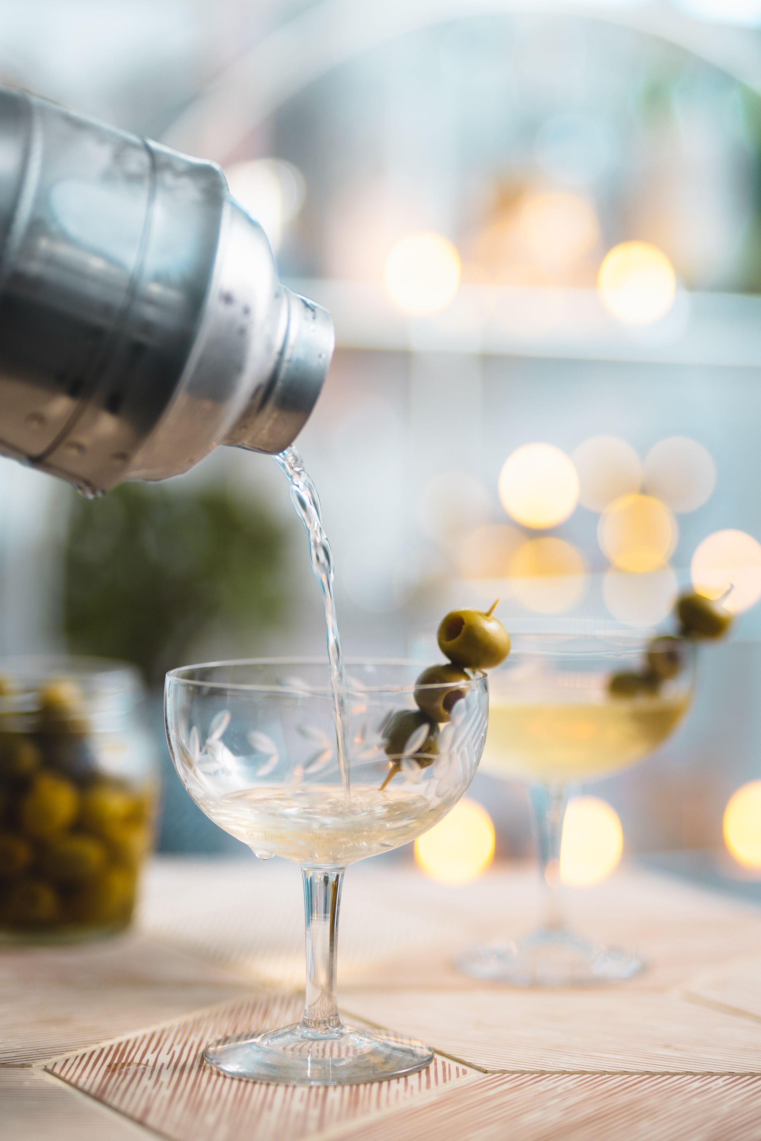将经典的伏特加马提尼酒从摇壶倒入装饰着绿橄榄的玻璃杯中