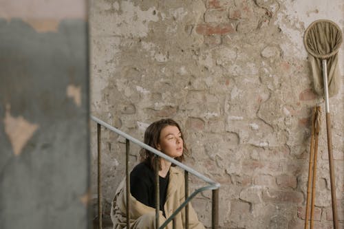Woman in Brown Jacket Leaning on Brown Concrete Wall