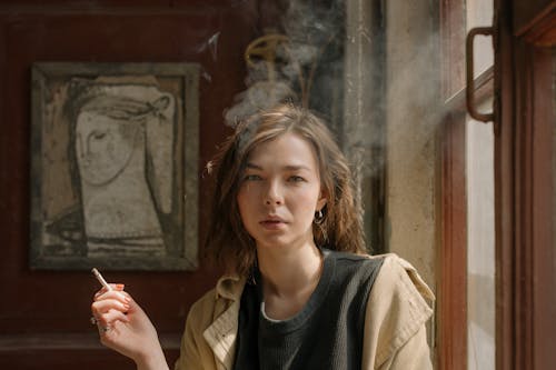 Woman in Black Crew Neck Shirt and Brown Coat Holding Cigarette Stick