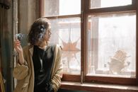一个穿着风衣的女人在阳光明媚的窗边，若有所思地在室内抽着烟