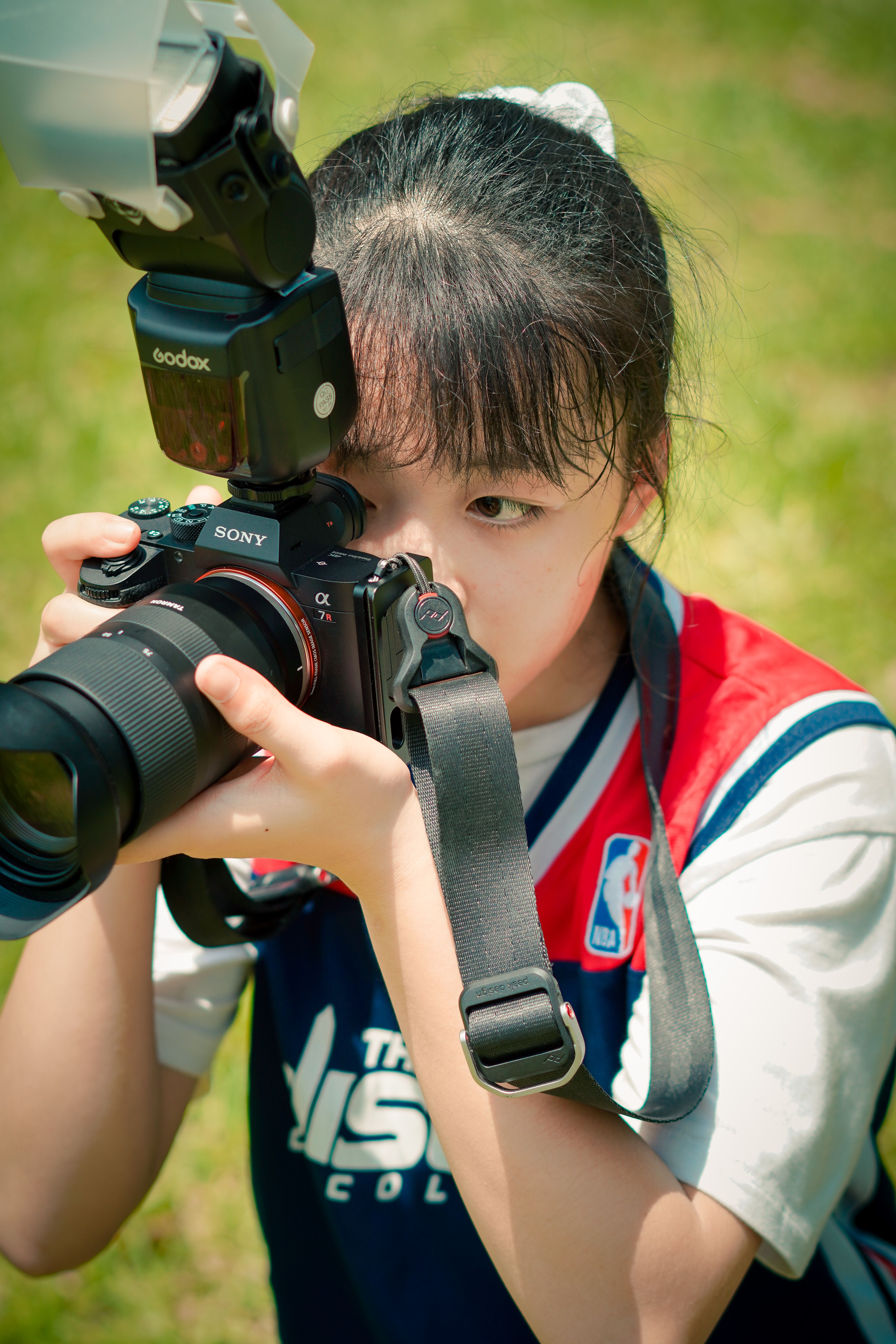 Young female in sportswear with ponytail holding professional photo camera on grassy field