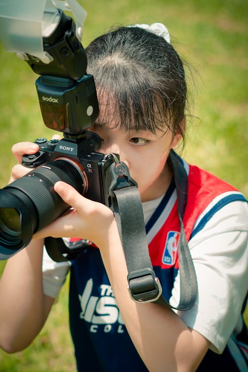 Young female in sportswear with ponytail holding professional photo camera on grassy field