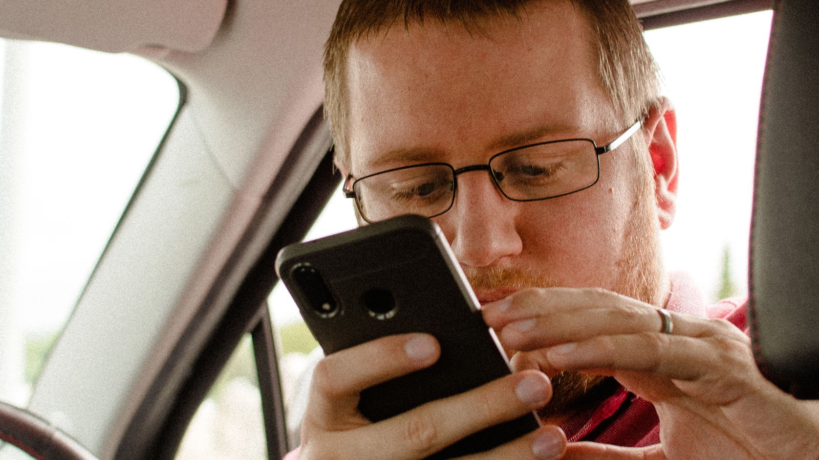 Vendedor conferindo uma mensagem de pagamento no celular dentro de um carro estacionado