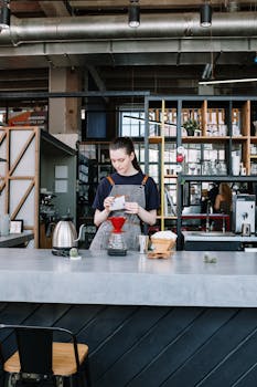 A female barista making pour over coffee in a stylish, urban café setting.