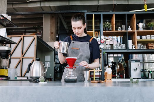 Young barista expertly making pour over coffee in a modern coffee shop interior.