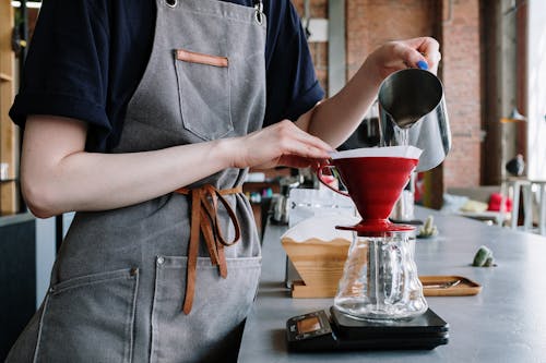 Person in Gray Apron Holding Red Ceramic Bowl