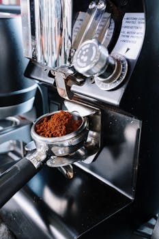 Detailed view of a coffee grinder with ground coffee in portafilter, professional café setting.