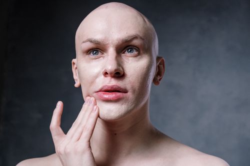 Free A bald man applies makeup in a studio setting, focusing on skincare and beauty routines. Stock Photo