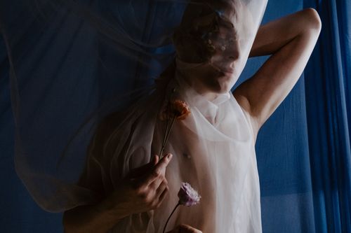 Free A creative portrait featuring a person with delicate floral elements and veil on a blue background. Stock Photo