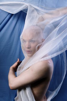 在蓝色背景下，一位秃头男子的艺术肖像被流动的透明织物包裹，展现出优雅的风姿