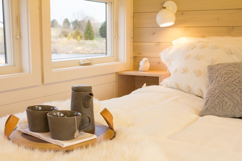 A white bed by a window with a tea tray, in a warm timber-lined room
