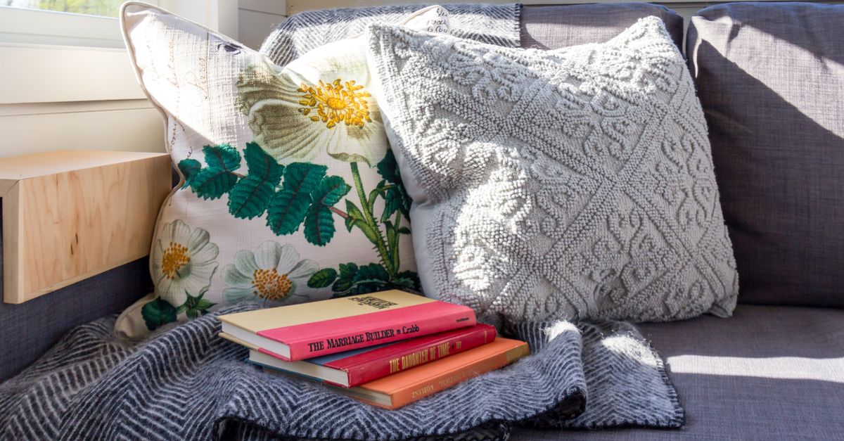 Close-up shot of a textured nook with a knitted blanket, a ribbed ceramic vase, a stack of art books, and a wooden tray