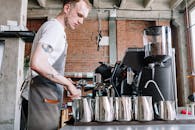 在砖墙风格的现代工业风咖啡馆里，一位年轻的男咖啡师正在准备咖啡