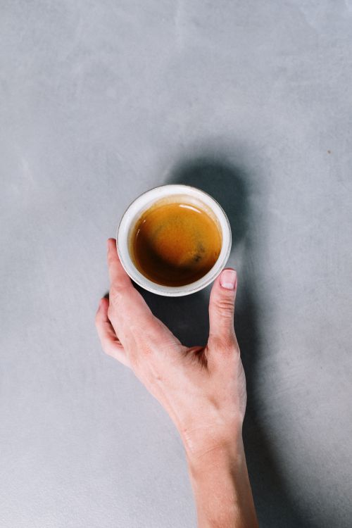 Free Close-up of a hand holding an espresso cup from above on a grey concrete surface. Stock Photo