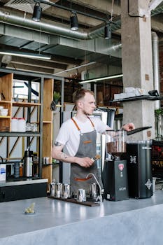 A young male barista prepares coffee in a stylish and modern café interior.