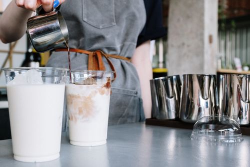 Free Close-up of a barista crafting iced lattes in a trendy indoor café setting. Stock Photo