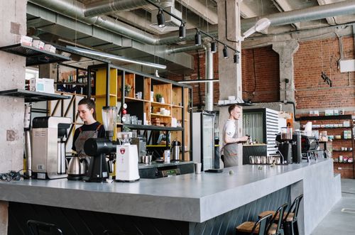 Free Baristas working in a trendy industrial-style coffee shop with exposed brick and beams. Stock Photo