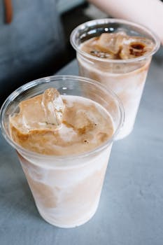 Two iced lattes in plastic cups with ice on a table, perfect for a refreshing break.