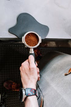 Overhead shot of a barista holding a portafilter filled with fresh ground coffee. Ideal for coffee culture themes.