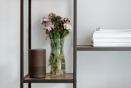 Розовые цветы в прозрачной стеклянной вазе на коричневой деревянной полке