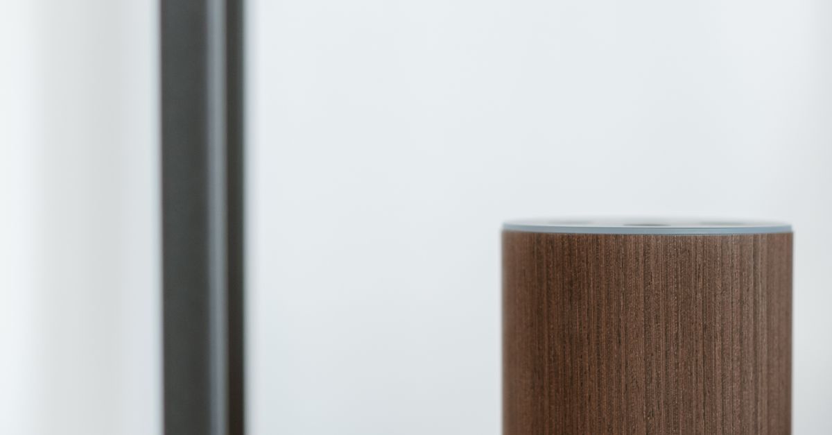 Photo by Anete Lusina A minimalist close-up of a smart speaker with a wooden finish, placed on a shelf indoors.